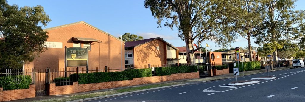 Front view of Corinda State High School with a fenced entrance, trees, and a sign indicating the administration office.