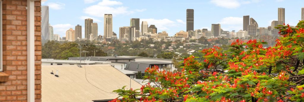 View of a city skyline with tall buildings, framed by greenery and vibrant flowers, offering a scenic urban landscape in Brisbane.