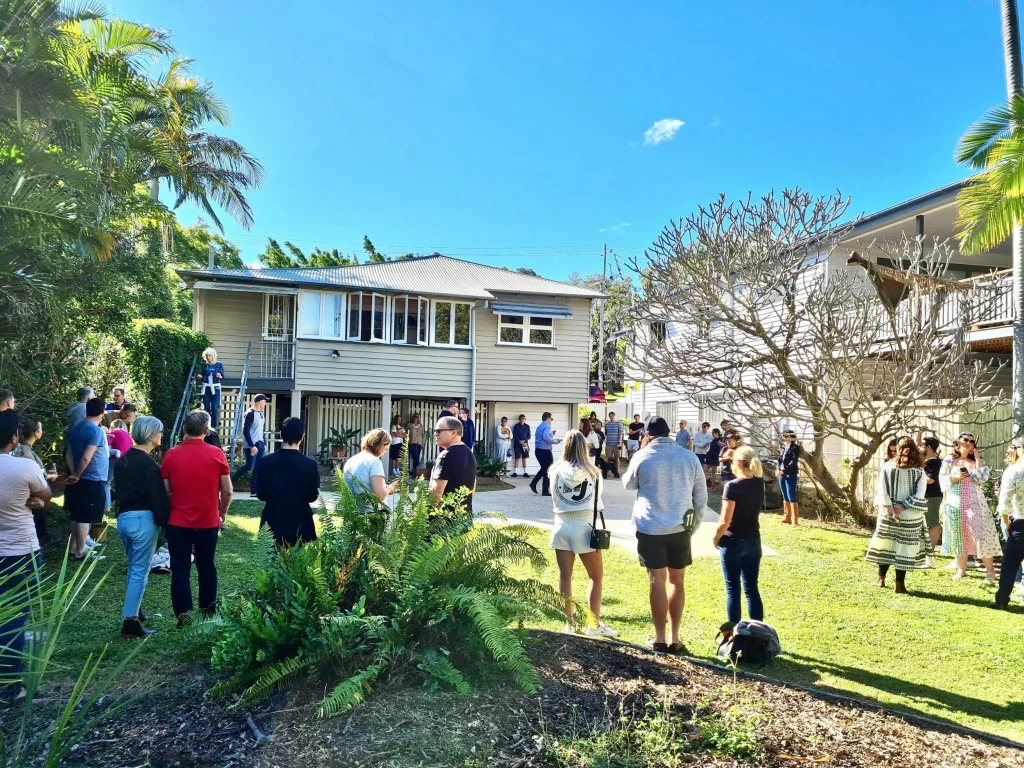 Property auction in Brisbane with buyers gathered around a residential home.