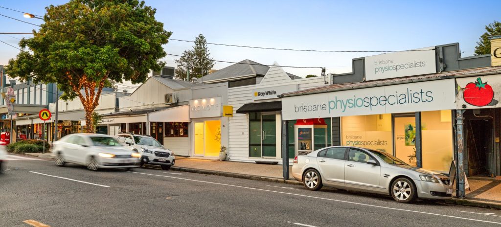 Wilston street view featuring shops, including Brisbane Physiotherapists, with cars and trees.