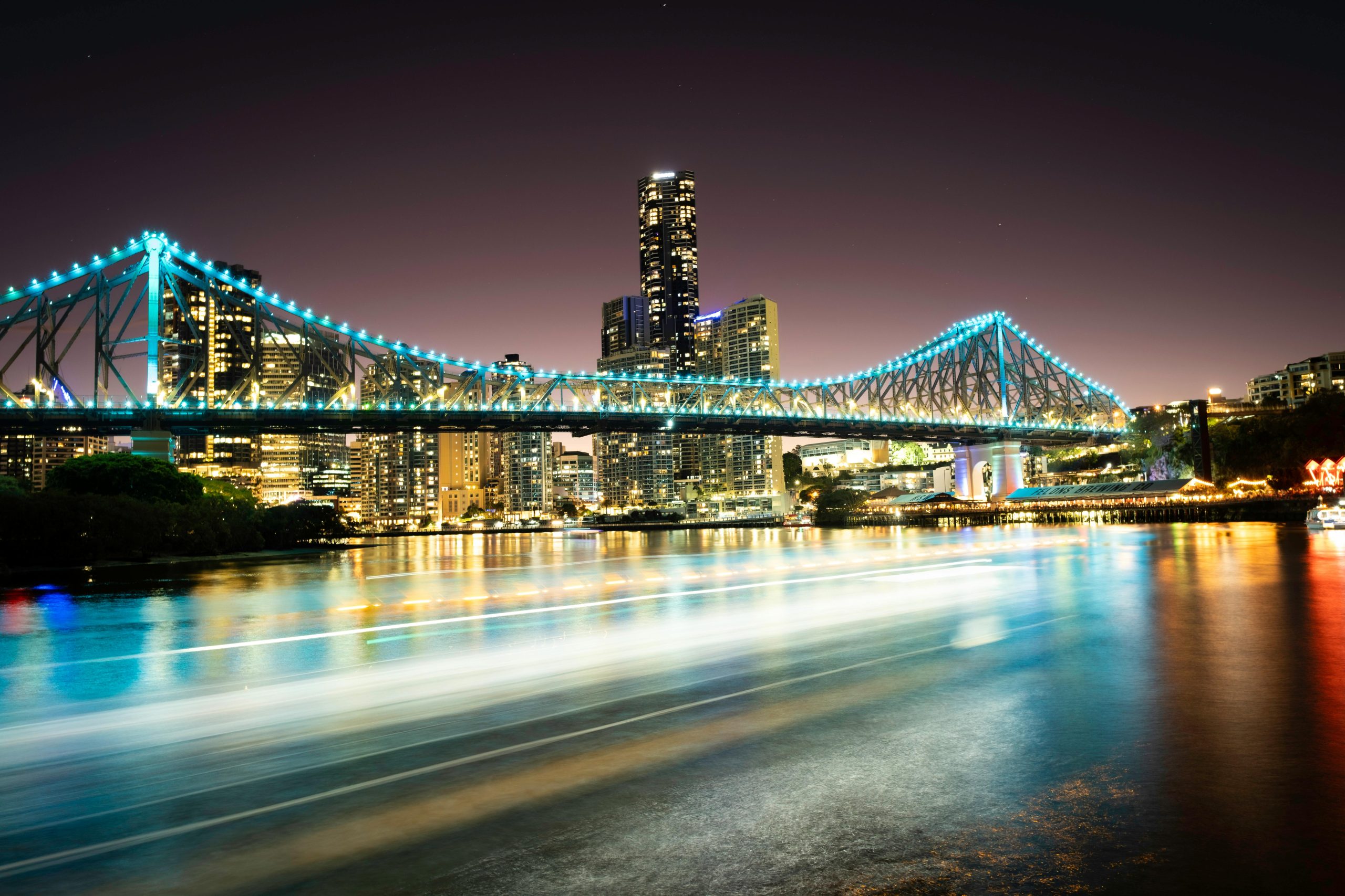 Brisbane City skyline at night with the Story Bridge illuminated, reflecting on the river in Queensland, Australia.