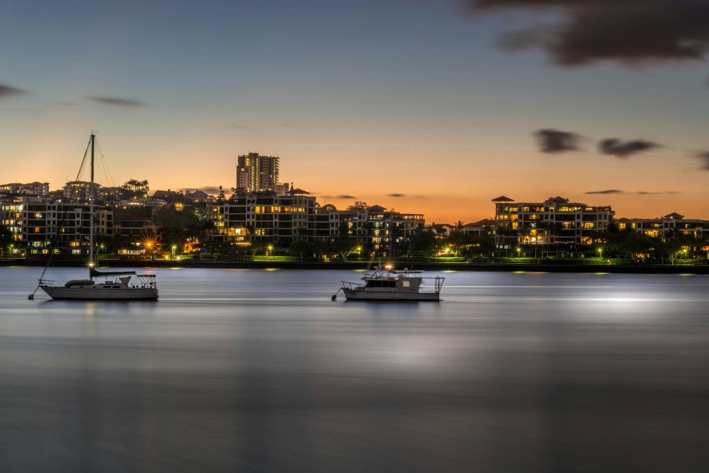 Sunset view of boats on the river with city buildings lit up in the background of Bulimba in Brisbane