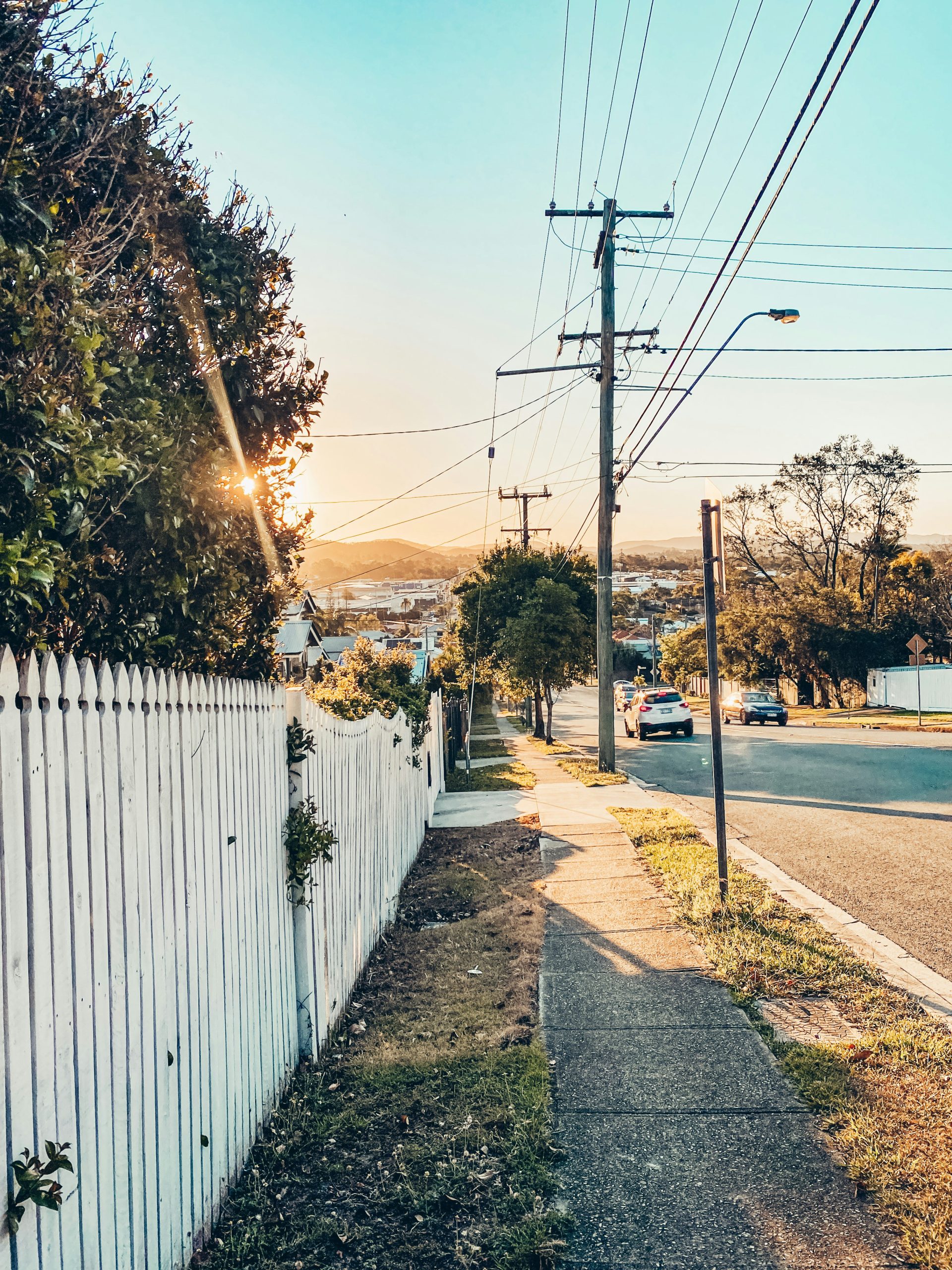 Residential street in Brisbane during sunset with a white picket fence and power lines.