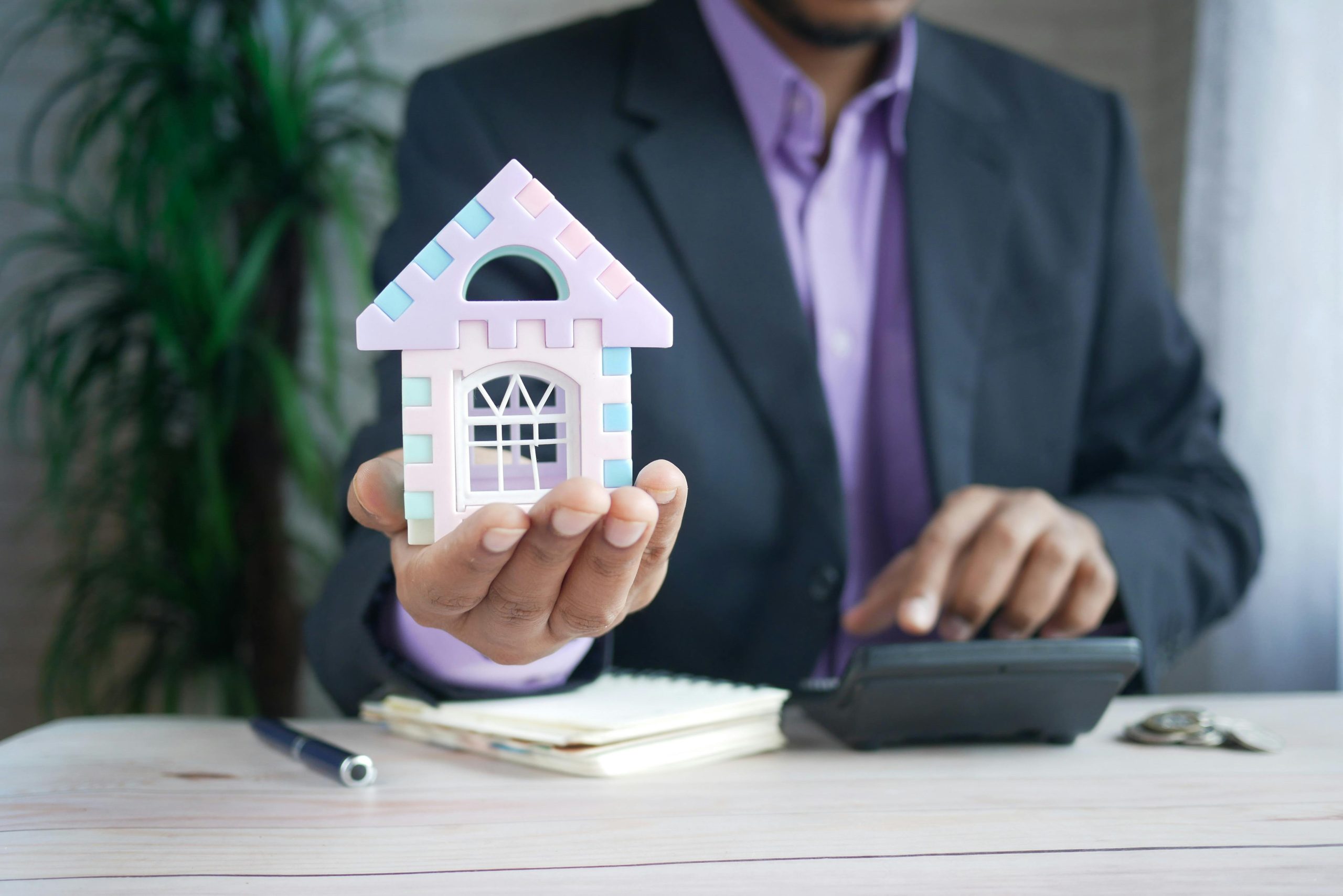 Property professional holding a small model house while using a calculator, representing finance planning for downsizing in Brisbane