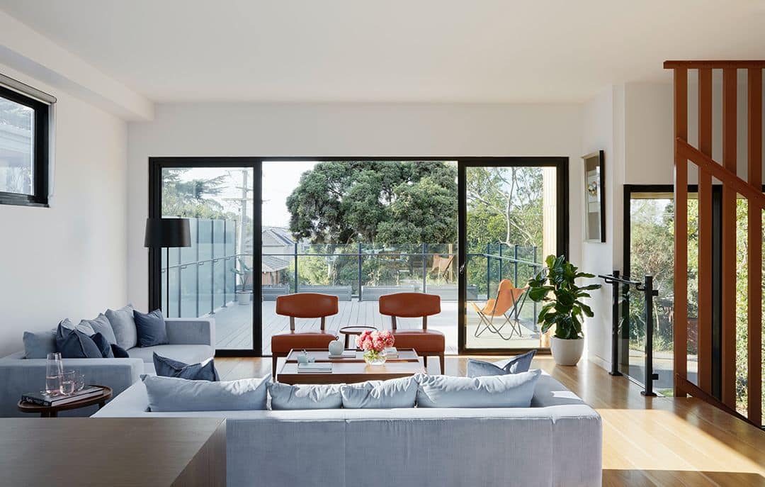 Modern house in Brisbane with a pool, balcony, and palm trees in the front yard.
