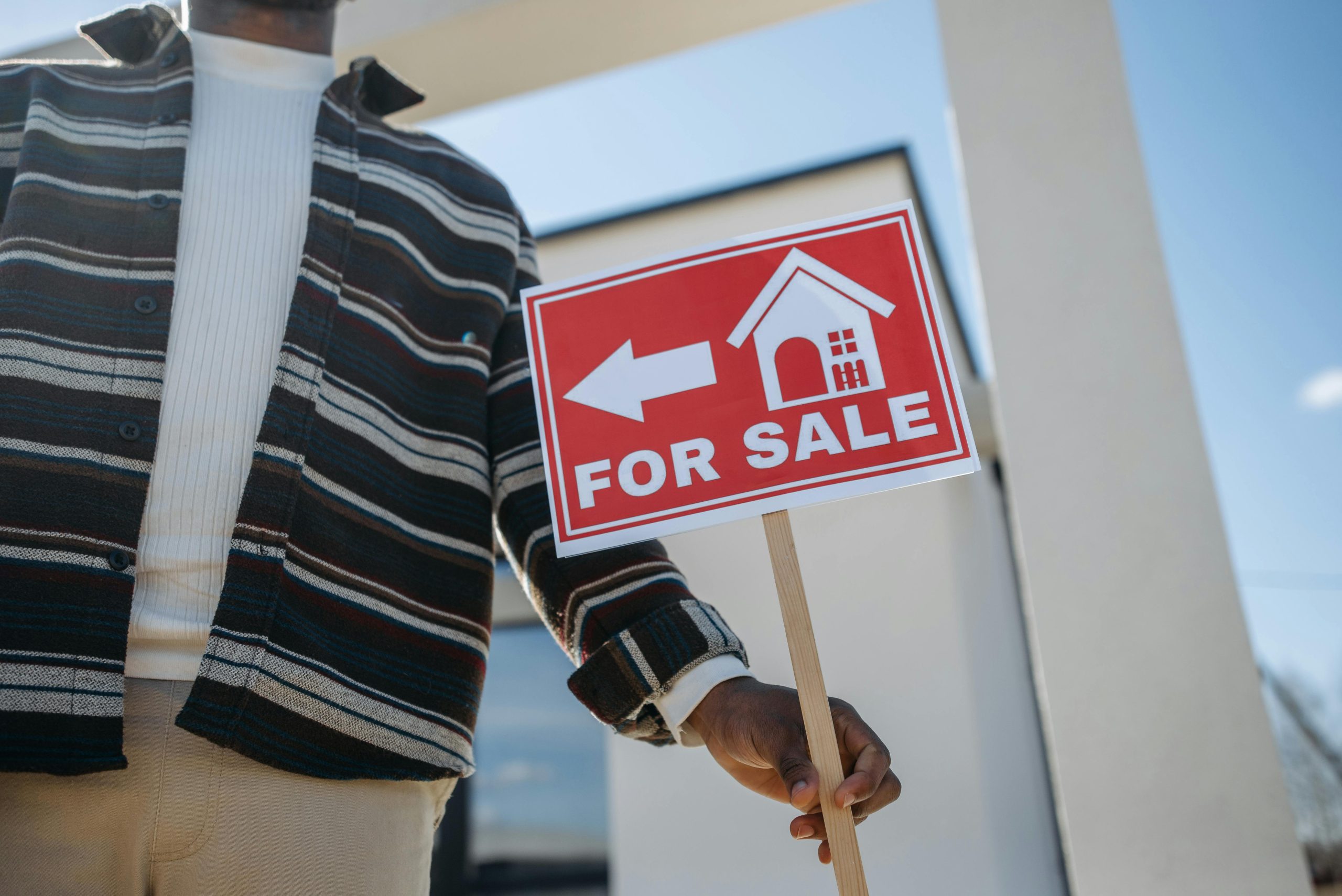 Person holding a red FOR SALE sign outside a home, representing selling a property for downsizing in Brisbane