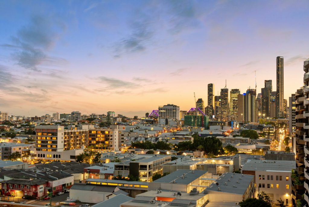 Brisbane skyline at sunset with city buildings, Story Bridge lights, and urban apartments in the foreground.
