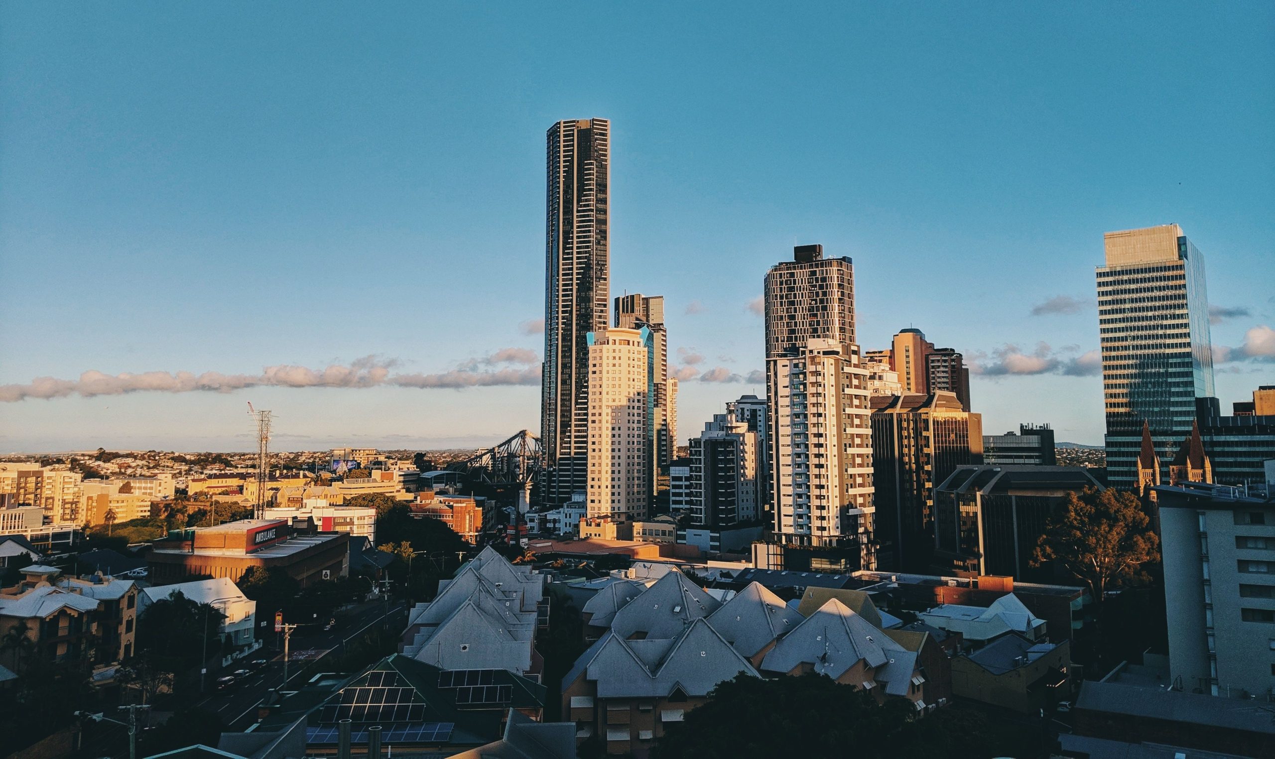 Brisbane city skyline with high-rise buildings and urban rooftops under a clear blue sky at golden hour.
