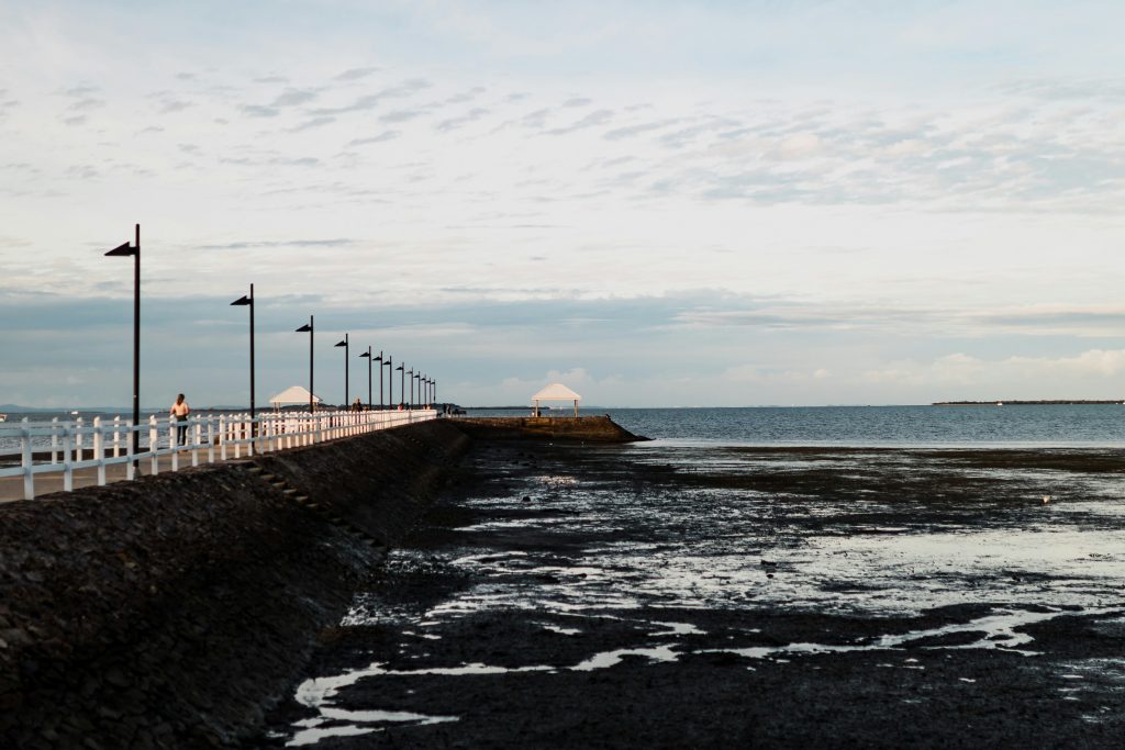 Wynnum QLD waterfront pier with white railings, black lamp posts, and low tide mudflats beside Moreton Bay