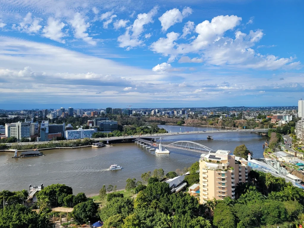 Aerial view of Brisbane QLD with the Brisbane River, city skyline, bridge, and blue cloudy sky.