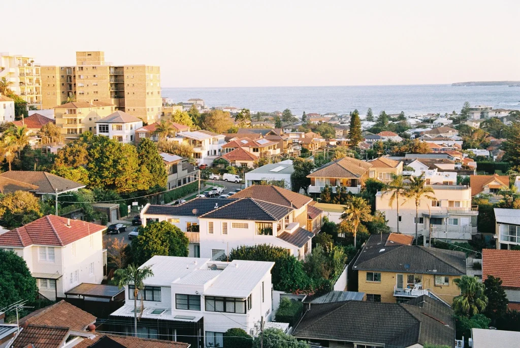Elevated view of houses in Brisbane city near the coastline with residential rooftops, apartment buildings, and ocean views.