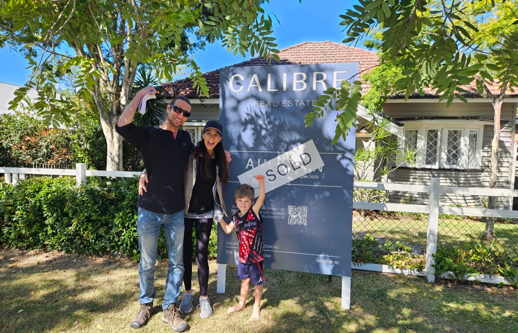 Happy family celebrating in front of a sold sign outside their new home in Brisbane.